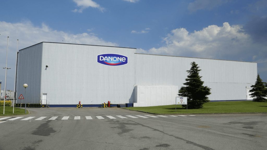 Danone logo on factory building, zebra crossing and grey road with tree, blue sky and clouds